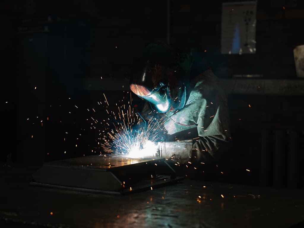 Welder mid-arc with sparks on a fabricated part